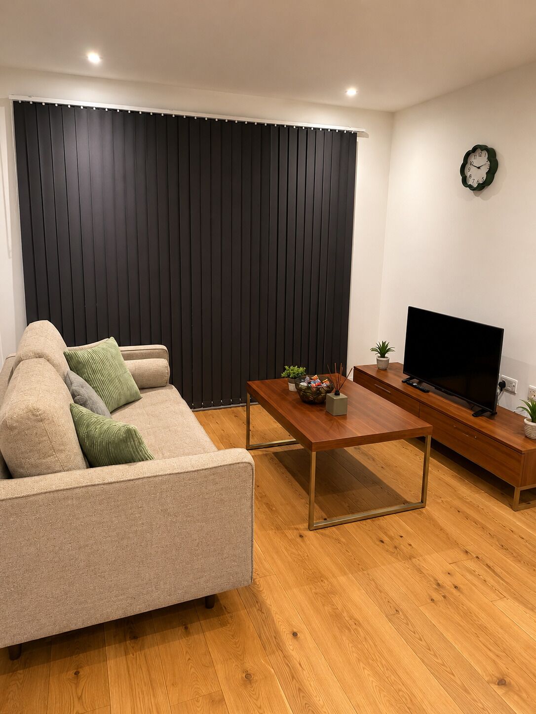 Una sala de estar con sofá, mesa de centro, mueble para televisión y un reloj en la pared.