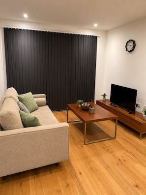 Ein Wohnzimmer mit einer Couch, einem Couchtisch, einer TV-Kommode und einer Wanduhr.