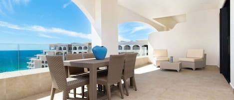 Un balcón con mobiliario de mimbre, un florero azul y vistas al mar y edificios.
