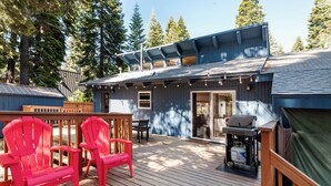 Eine Terrasse mit Holzhöckern, einem Grill und einem überdachten Bereich mit Schiebetür.