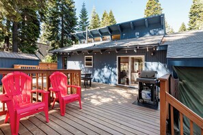 Eine Terrasse mit Holzhöckern, einem Grill und einem überdachten Bereich mit Schiebetür.