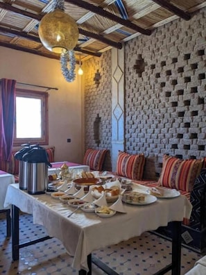 Un comedor con una mesa dispuesta para una comida, una lámpara colgante y una pared de ladrillo con un diseño geométrico.