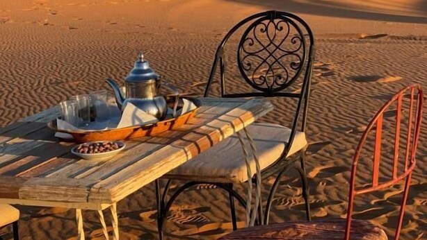 Escena desértica con una mesa puesta para una comida, una silla y otra silla de metal.