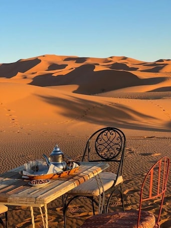 A desert scene with a table set for a meal, a chair, and a metal chair.. Moroccan Desert Camp