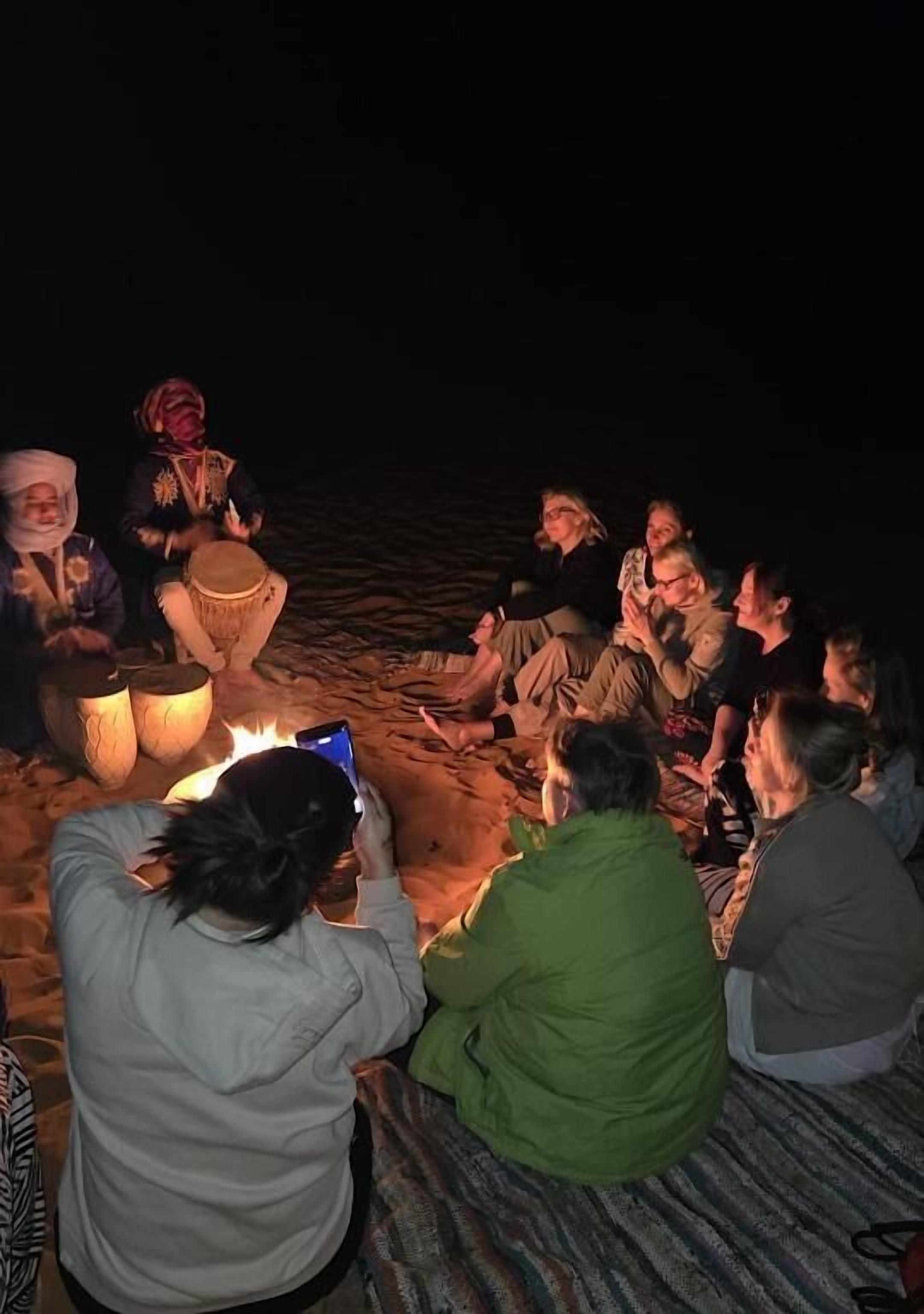 Eine Gruppe von Menschen sitzt am Abend an einem Lagerfeuer.