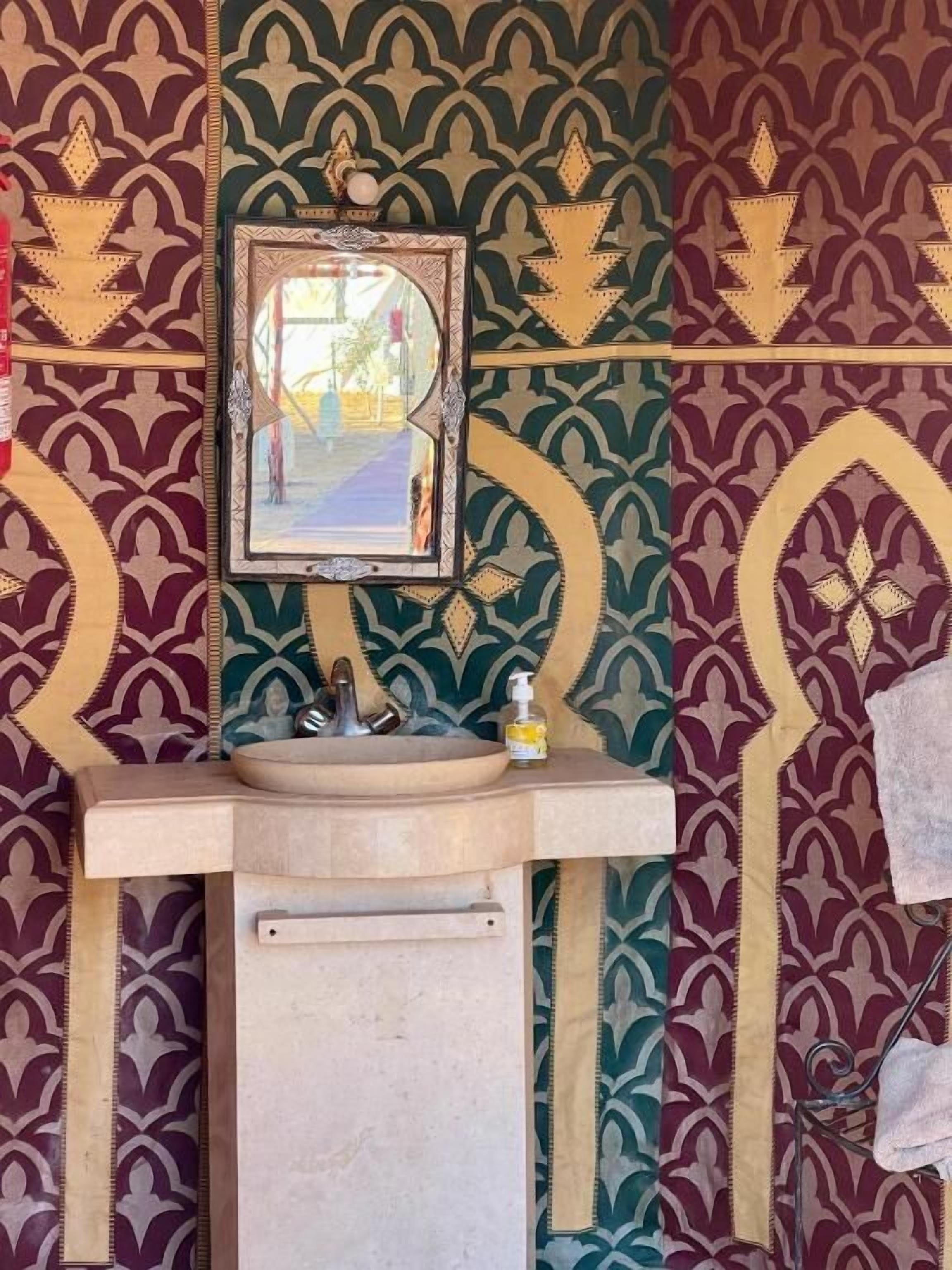 A bathroom with a sink, mirror, and towel rack against a patterned wall.