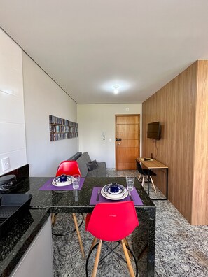 Una cocina moderna con comedor, encimeras de granito, horno empotrado, panel de pared de madera y un televisor de pantalla plana sobre una mesa de madera.