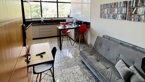 A modern kitchen with a dining area, a gray sofa, and a large window. - LK Lourdes 9 (Belo Horizonte)