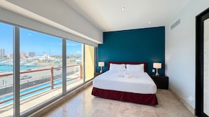 Ein Hotelzimmer mit einem großen Bett, zwei Nachttischlampen, Blick auf eine Marina und eine Stadtansicht.