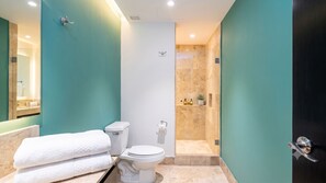 A modern bathroom with teal walls, a white toilet, a glass shower enclosure, and a towel rack. - Stylish 2BR Condo at Deck 12 Puerto Vallarta (Puerto Vallarta)