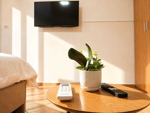 A hotel room with a bed, a TV mounted on the wall, a potted plant, a remote control, and a small table. - 2BR Near Beach  Big Terrace Free Parking (Golem)