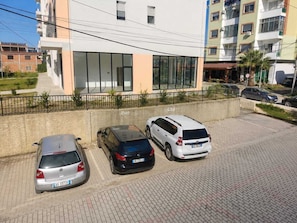 Ein Parkplatz mit drei parkenden Autos vor einem Gebäude mit großen Fenstern und einer Betonbarriere.