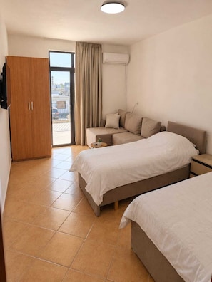 A hotel room with a bed, a sofa, a small table, a wardrobe, and a sliding glass door to the outside. - 2BR Near Beach Big Terrace Free Parking (Golem)