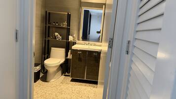 Un baño con inodoro, lavabo y estantes con artículos de aseo.