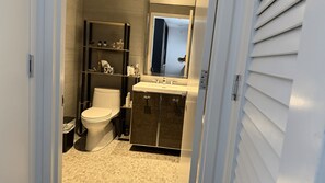 A bathroom with a toilet, sink, and shelves with toiletries.