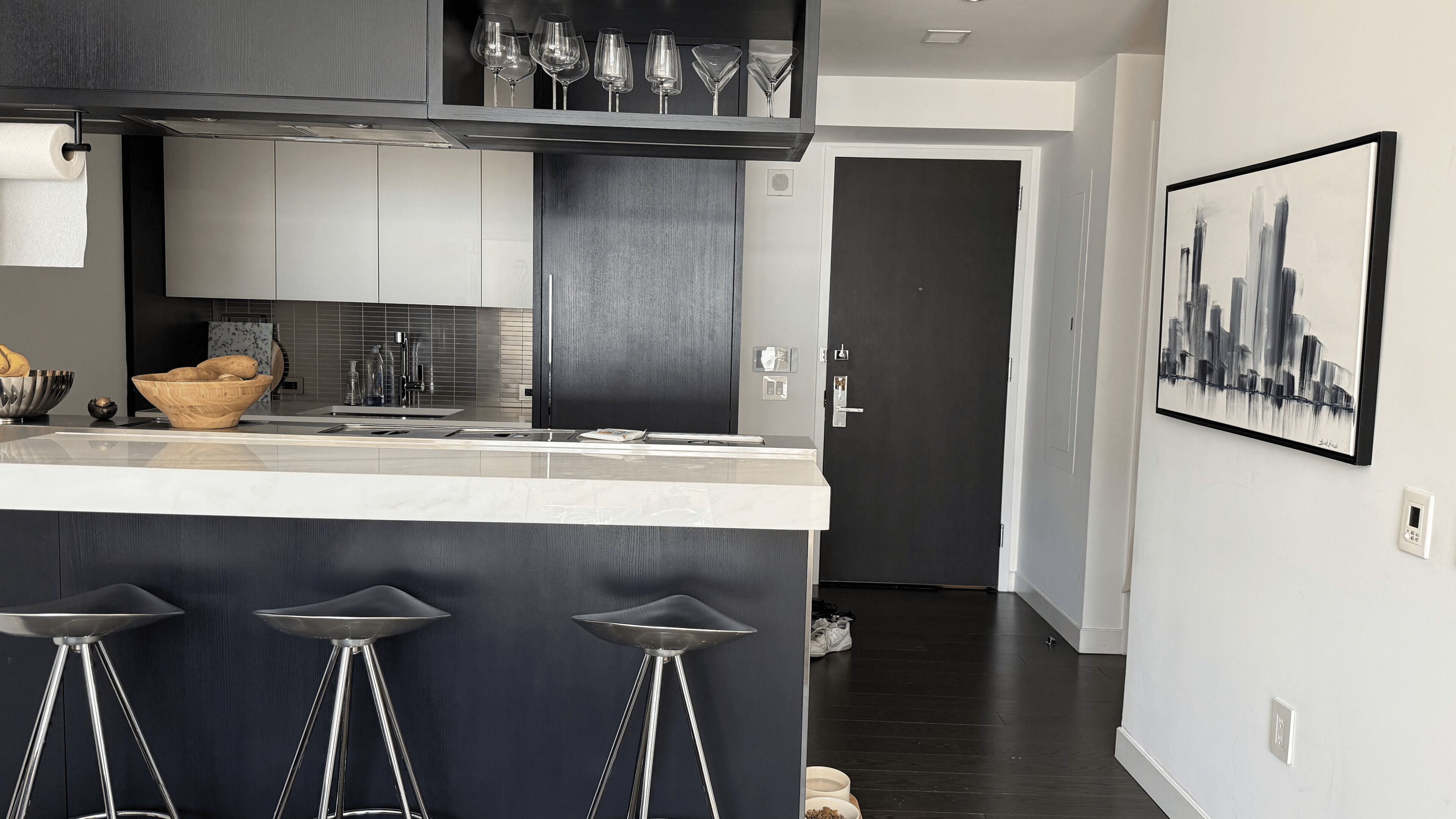 Cocina moderna con barra, electrodomésticos de acero inoxidable y un cuadro de paisaje urbano.