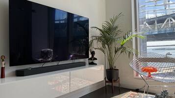 A modern living room with a large flat-screen TV, a potted plant, a decorative chair, and a small statue.