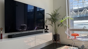 A modern living room with a large flat-screen TV, a potted plant, a decorative chair, and a small statue.