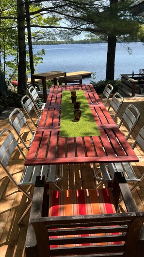 Une table de pique-nique en bois avec des chaises en métal, un tapis vert et une vue sur un lac.