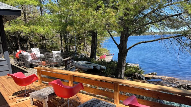 Une terrasse en bois avec des chaises rouges, une table et une vue sur un lac.