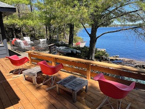 Um deck de madeira com cadeiras vermelhas, uma mesa e vista para um lago.