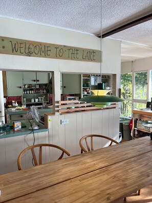 Une cuisine avec une pancarte indiquant « Bienvenue au bord du lac », des armoires en bois, un ventilateur et un coin repas avec des chaises.
