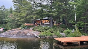 Una cabaña junto al lago con un muelle, rodeada de un bosque denso.