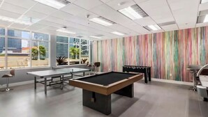 Een pooltafel, een tafelvoetbaltafel en een pingpongtafel in een ruimte met grote ramen en een gestreepte muur.