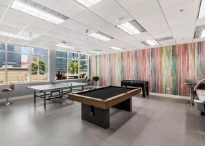 A pool table, foosball table, and a table tennis table in a room with large windows and a striped wall. - Breathtaking Condo at Club at Brickell Bay 16 Floor (Miami)