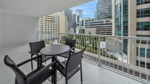 Een balkon met een tafel en stoelen, met uitzicht op een stadsgezicht met moderne gebouwen.