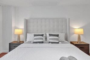 Une chambre à coucher avec une tête de lit capitonnée, deux tables de chevet avec des lampes, un lit avec une literie blanche et deux oreillers à motifs rayés.