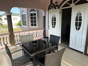 An outdoor patio with a table and chairs, a white door, and a view of the surrounding area. - Runaway Dreams Jamaica – Your Private Paradise Awaits (Runaway Bay)