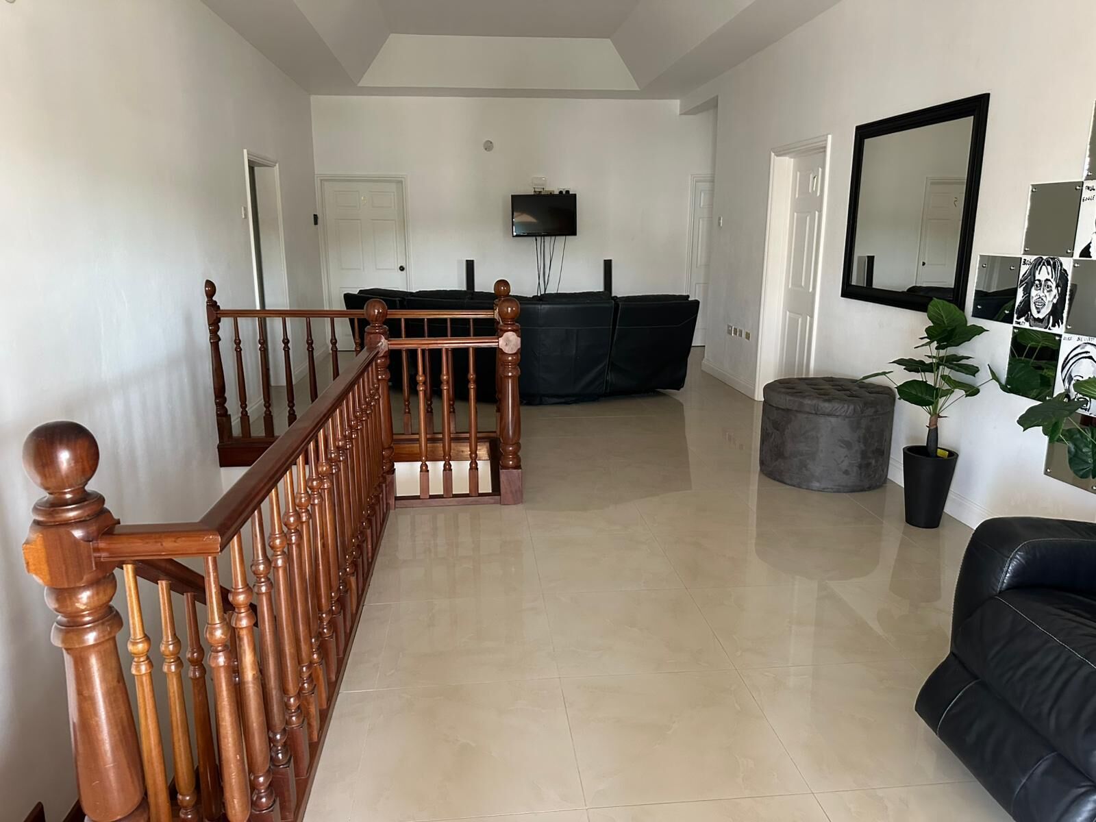 A spacious living area with a wooden staircase, a black leather sofa, a flat-screen TV, and a potted plant.