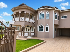 A large, multi-story house with a curved balcony, a well-maintained lawn, and a gated entrance. - Runaway Dreams Jamaica – Your Private Paradise Awaits (Runaway Bay)