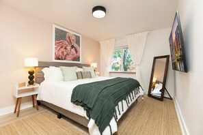 Une chambre à coucher comprenant un lit, des tables de chevet, un miroir, une fenêtre avec des rideaux et des œuvres d’art accrochées aux murs.
