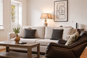 Un salon avec un canapé, une table basse, une lampe et une œuvre d’art encadrée accrochée au mur.