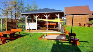 A wooden pavilion with benches and picnic tables in a grassy backyard.