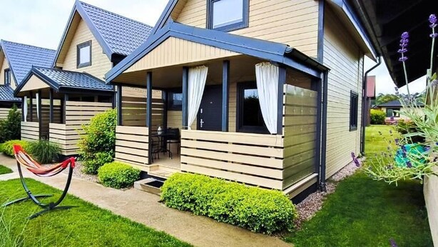 Een rij moderne vakantiehuisjes, elk met twee verdiepingen, een overdekte veranda en een verzorgde tuin.