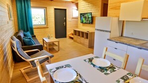 Een houten hutje met een bank, een eettafel gedekt voor twee personen, een televisie en een keuken.
