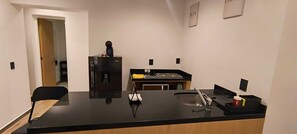 Eine Küche mit schwarzem Arbeitsplatz, einer Kaffeemaschine, einem Spülbecken und einem Kühlschrank.