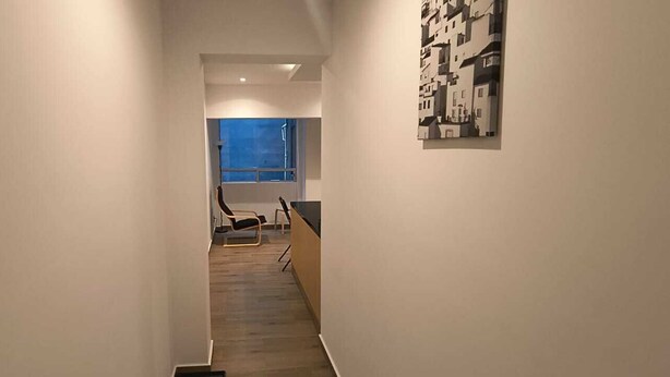 A narrow hallway with a wooden floor, a chair, and a window with a view of the sky. - Sevillavenue (Ciudad de México)