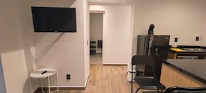 Eine kompakte Küche mit Kühlschrank, einem an der Wand montierten Fernseher und einer kleinen Essecke mit einem Stuhl.