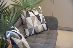 Ein graues, gepolstertes Sofa mit einem geometrisch gemusterten Kissen und einem Streifenmuster-Kissen.