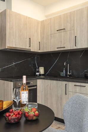 Eine moderne Küche mit Holzschränken, einer schwarzen Marmorarbeitsplatte, einer Kaffeemaschine und einer Weinflasche.