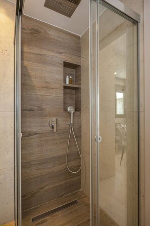 Eine barrierefreie Dusche mit Glastür, einer Wand aus Holzverkleidung und einem integrierten Ablagebereich für Toilettenartikel.