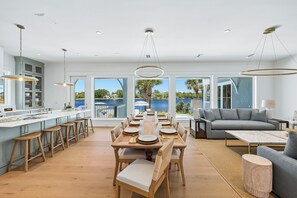 Eine geräumige Küche mit einer großen Kochinsel, ein Essbereich mit langem Tisch und ein Wohnzimmer mit Sofa und Couchtisch.