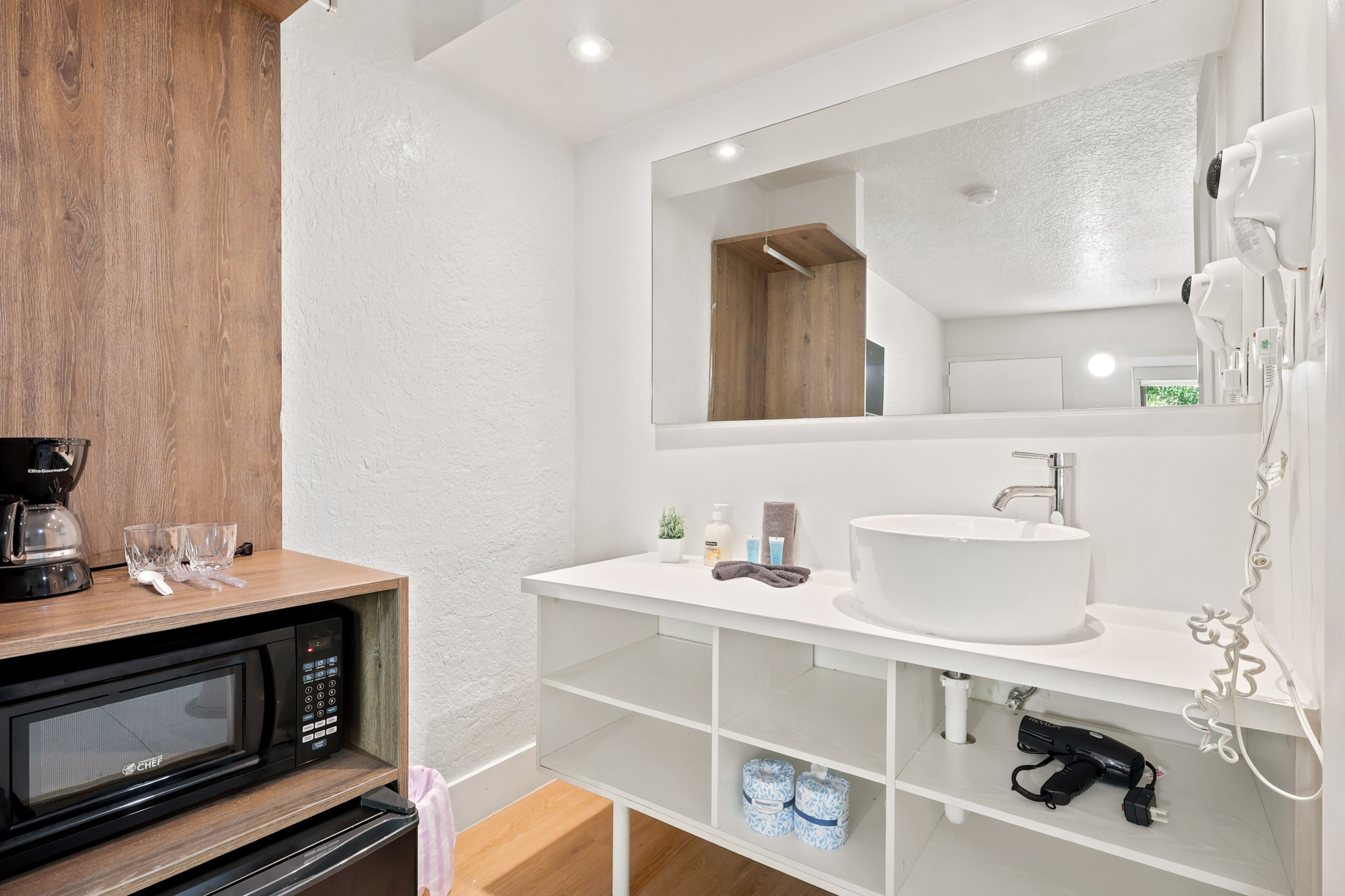 Une salle de bain moderne avec un lavabo blanc, un grand miroir, un sèche-cheveux et un four à micro-ondes.