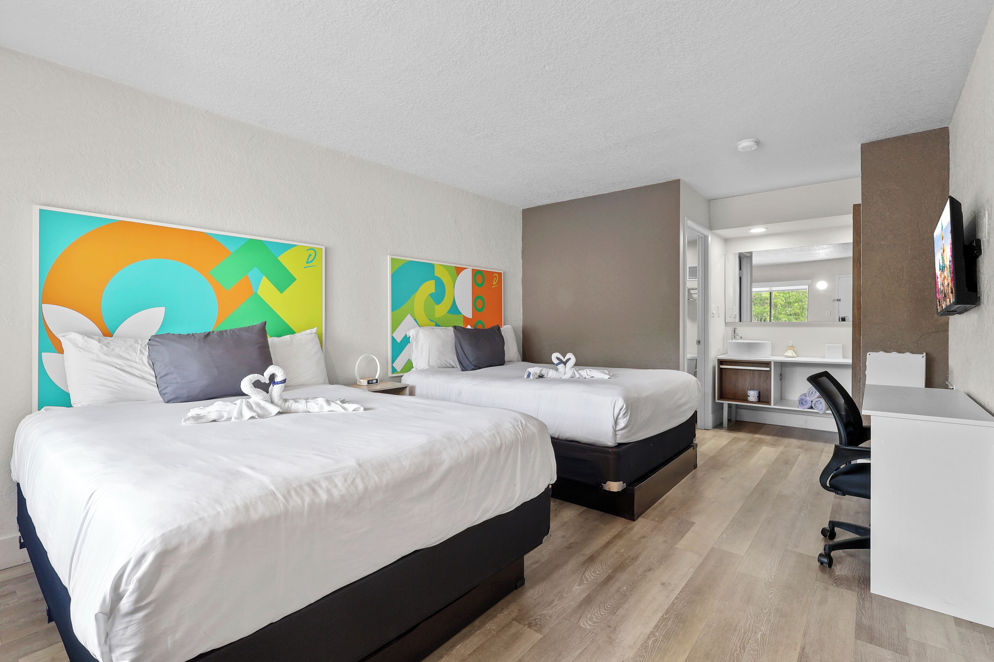 Habitación de hotel con dos camas, un escritorio, una silla y un televisor.