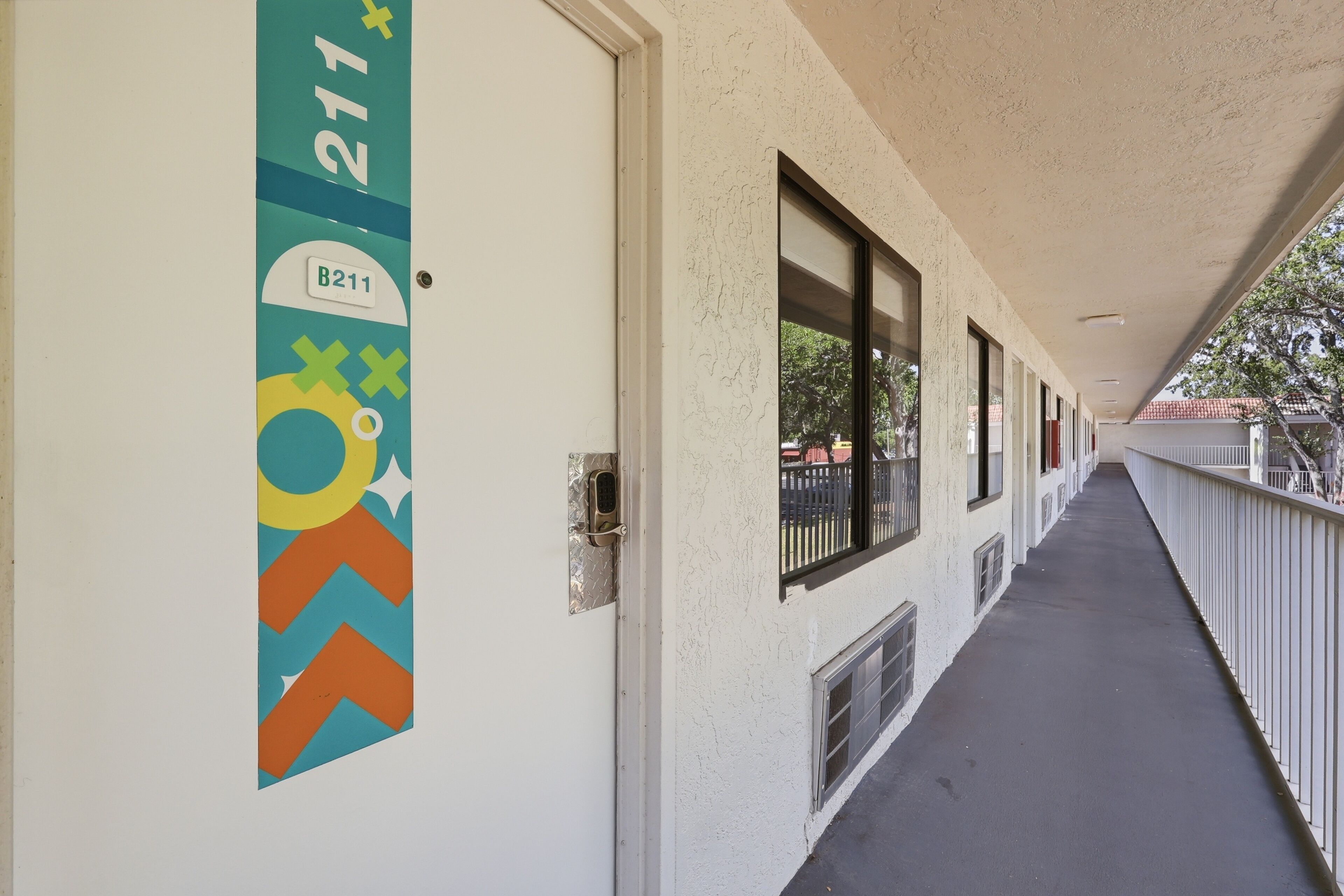 Un couloir avec une porte portant l’inscription « B211 » et un panneau à motifs en forme de chevrons.