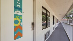 A corridor with a door labeled 'B211' and a chevron-patterned sign. - Budget Disney Room Pool & Parking (Kissimmee)